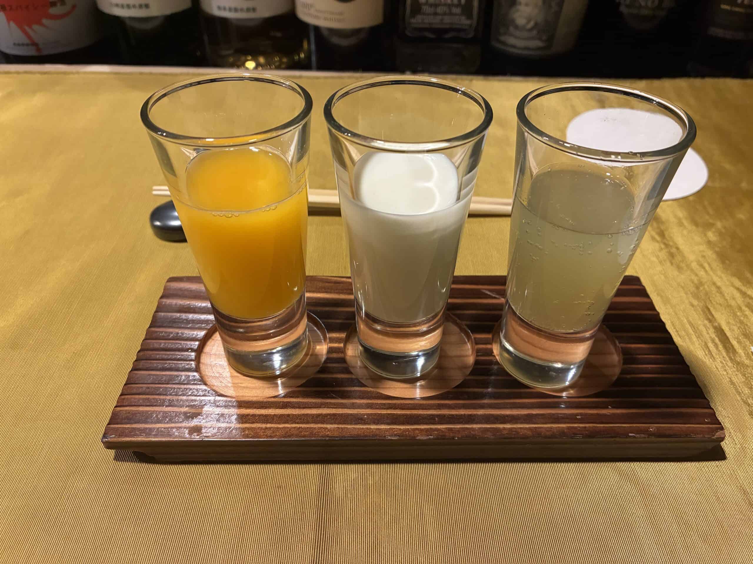 木のトレーに並んだ3杯のドリンク。左からオレンジジュース、牛乳、酢橘キウイソーダ