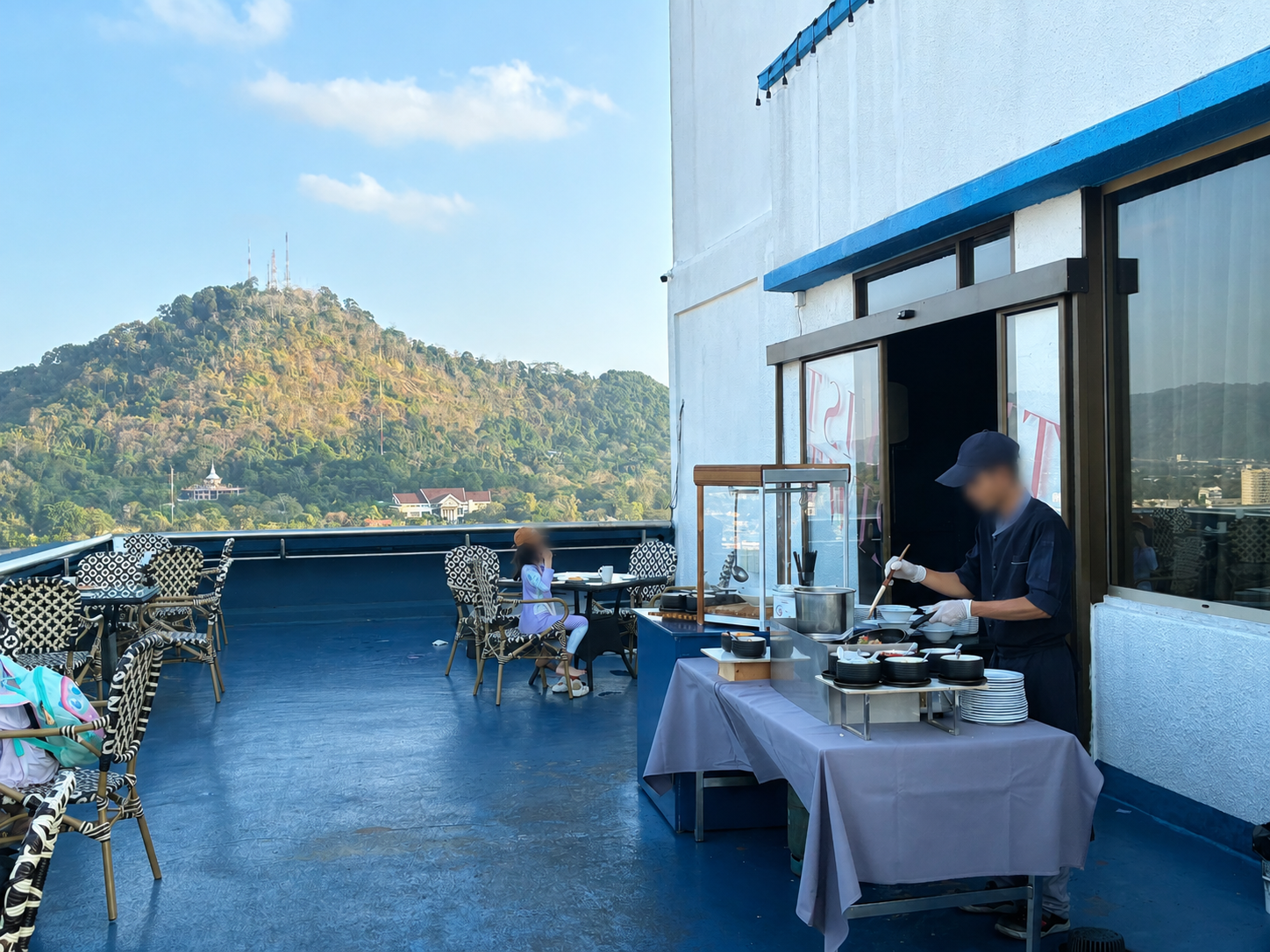 ホテル屋外テラス席。奥にKhao Rangの丘が見え、シェフが卵料理を調理している
