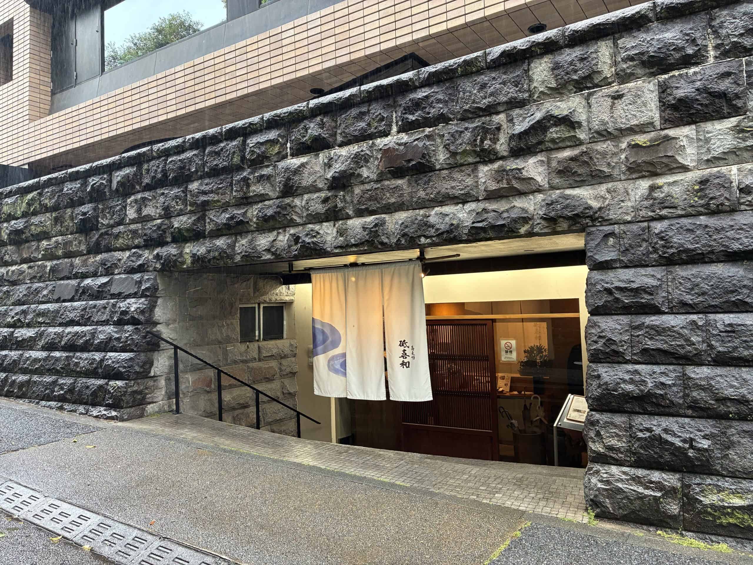 雨の日の蕎麦切 砥喜和の入口。石積みの壁と白い暖簾が印象的