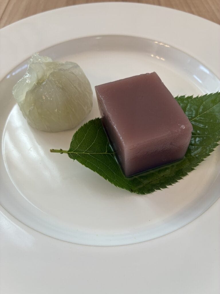 一幸庵の水羊羹と葛饅頭「緑陰」。青い葉を敷いた白い器に、澄んだ小豆色の水羊羹と葛の白い饅頭