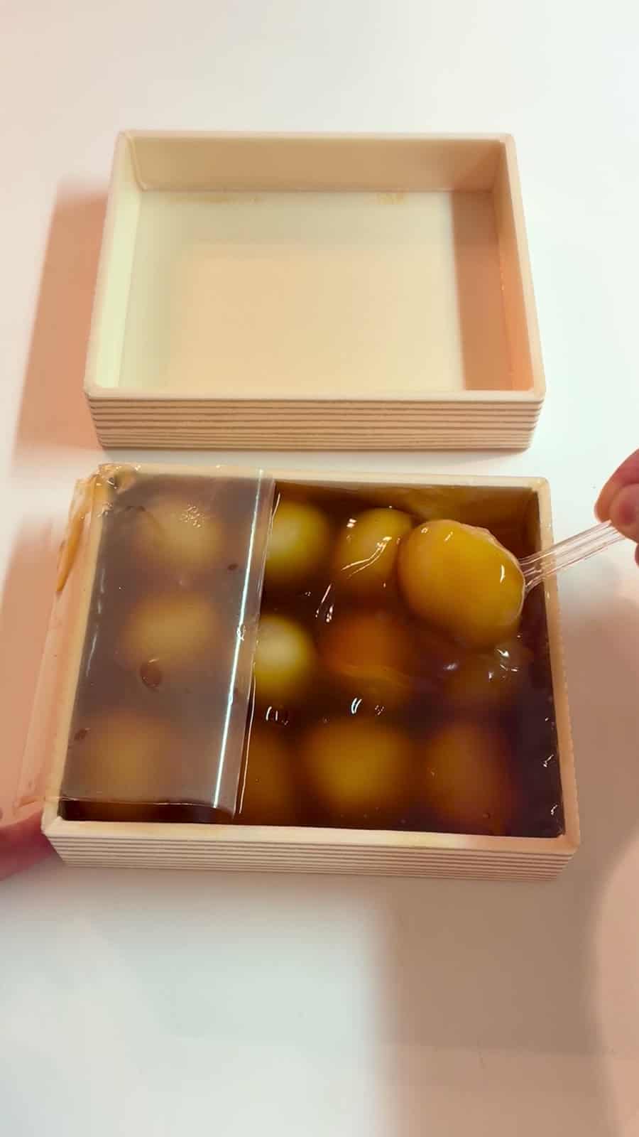 木箱を開け、たれに浸かった団子をスプーンで持ち上げているところ