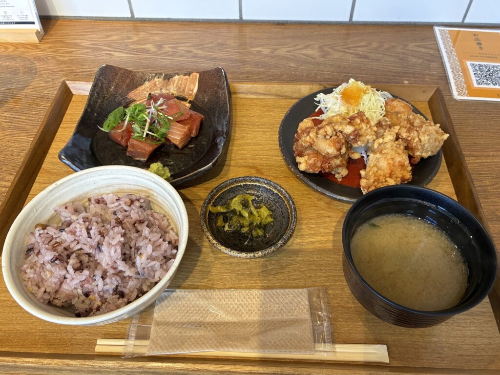 お刺身と唐揚げの定食。ご飯、お味噌汁、小鉢が木のトレーに並んでいる