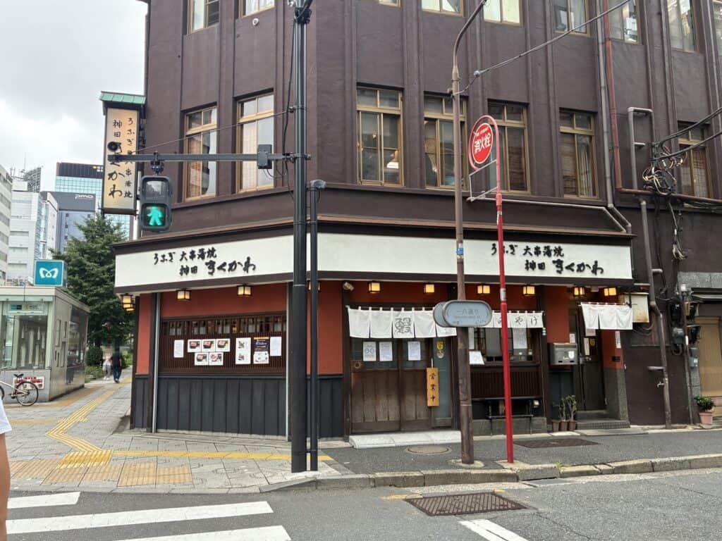 交差点の角に立つ神田きくかわ神田店の外観。「うなぎ 大串蒲焼」の看板とのれんが見える