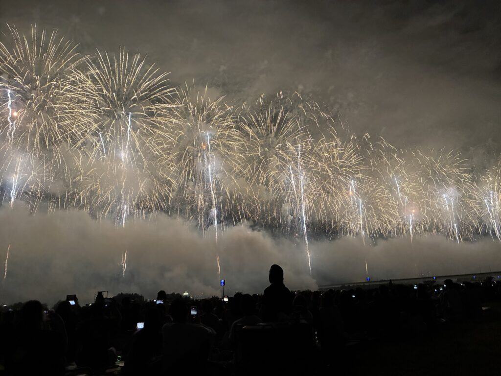 夜空いっぱいに広がる長岡花火。マス席から見上げる観客のシルエット