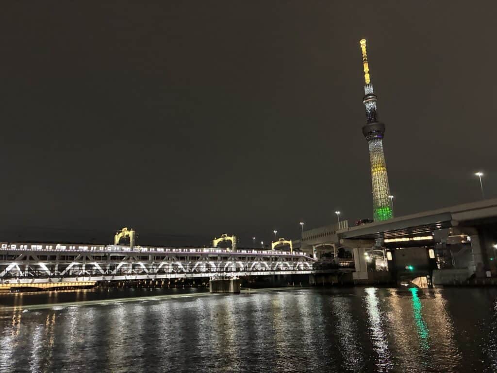 隅田川の水面越しに見える夜のスカイツリーと橋