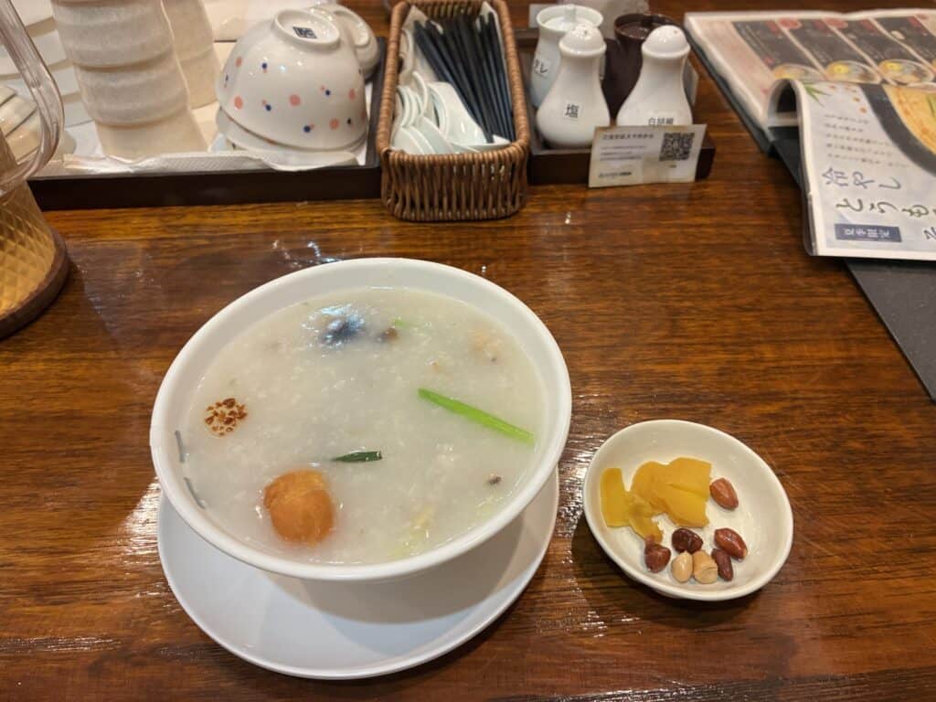白い器に入ったとろとろの香港粥と、お漬物と揚げ落花生の小皿