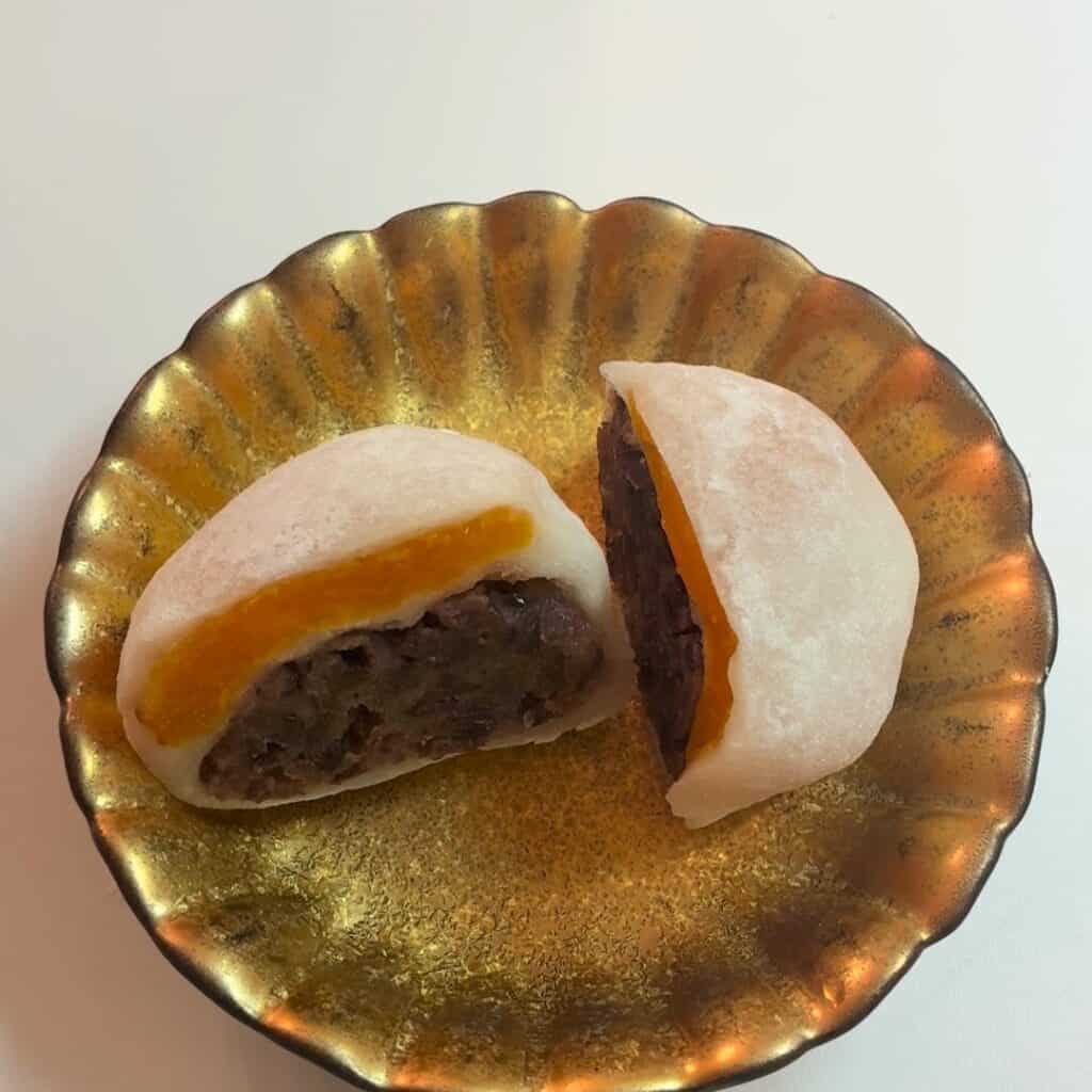 金の皿にのったあんず大福 の断面。オレンジ色のあんずと餡が見える