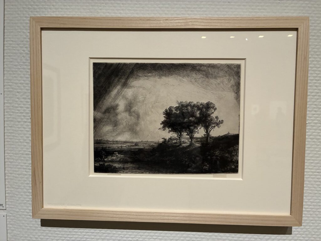 額装されたレンブラントの風景版画。木立の上の空が斜めの線で描かれている
