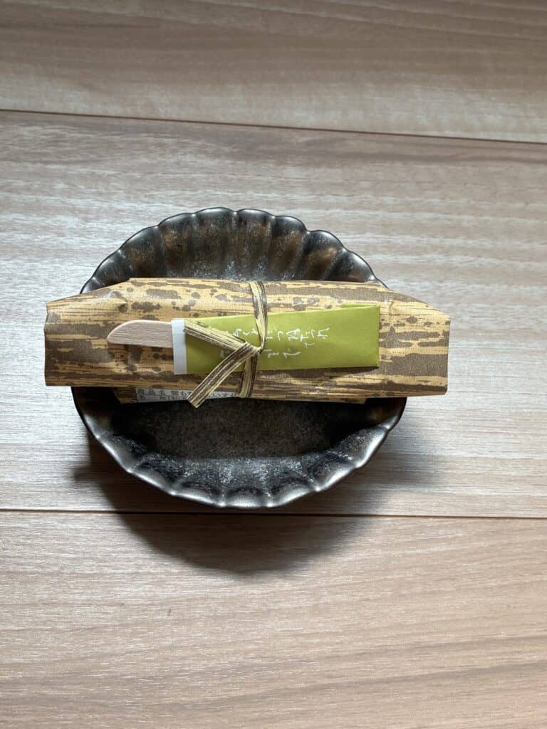 竹の皮のような包みに緑の掛け紙と木のへらが付いた鶯もち