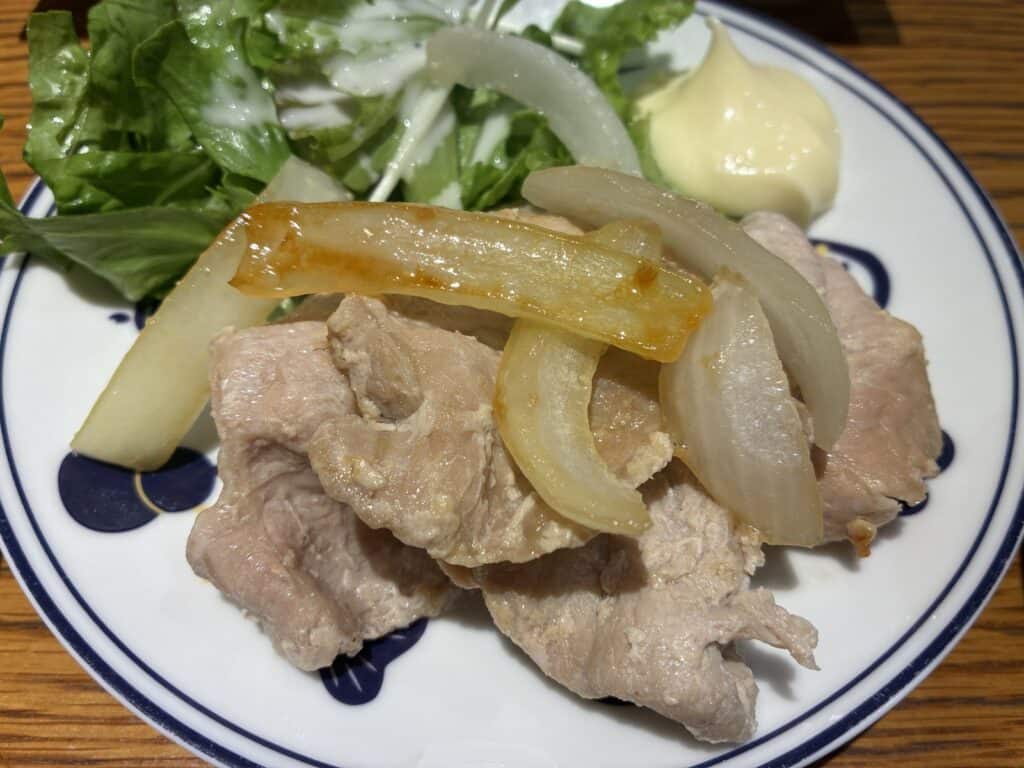 玉ねぎと一緒に炒めた豚ロースとサラダが盛られた皿
