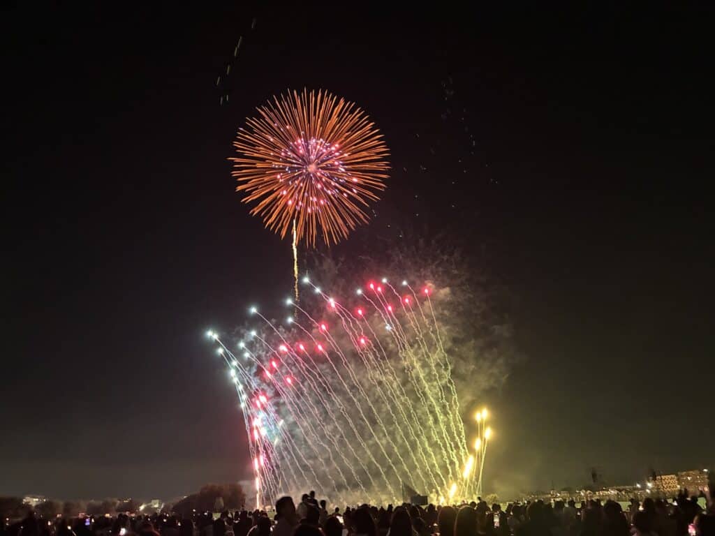 赤い大輪の花火と、その下で扇のように広がる色とりどりの仕掛け花火