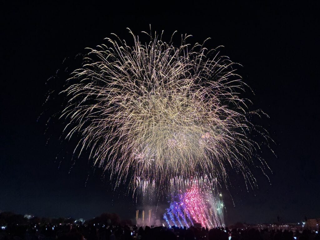 金色の花火の下で、青や紫の仕掛け花火が光っている